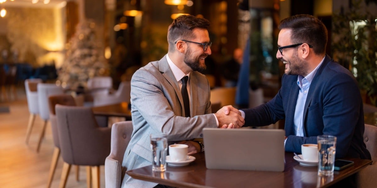 Two businessman sitting at a table shaking hands